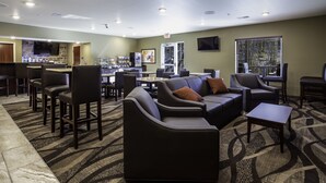 A hotel lobby with a bar area, seating arrangements, and a television. - Cobblestone Inn & Suites - Brookville (Brookville)