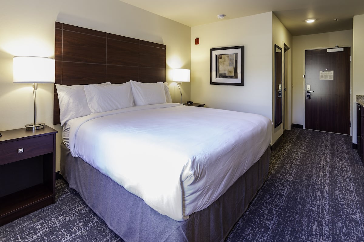 A hotel room with a large bed, two bedside lamps, a framed picture on the wall, and a door with a sign.