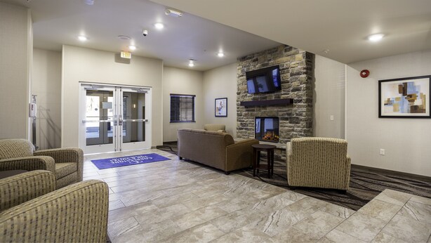 A lobby with a stone fireplace, seating area, and an exit door. - Cobblestone Inn & Suites - Brookville (Brookville)