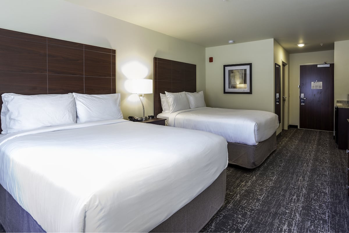 A hotel room with two beds, a desk, a lamp, and a small kitchenette.