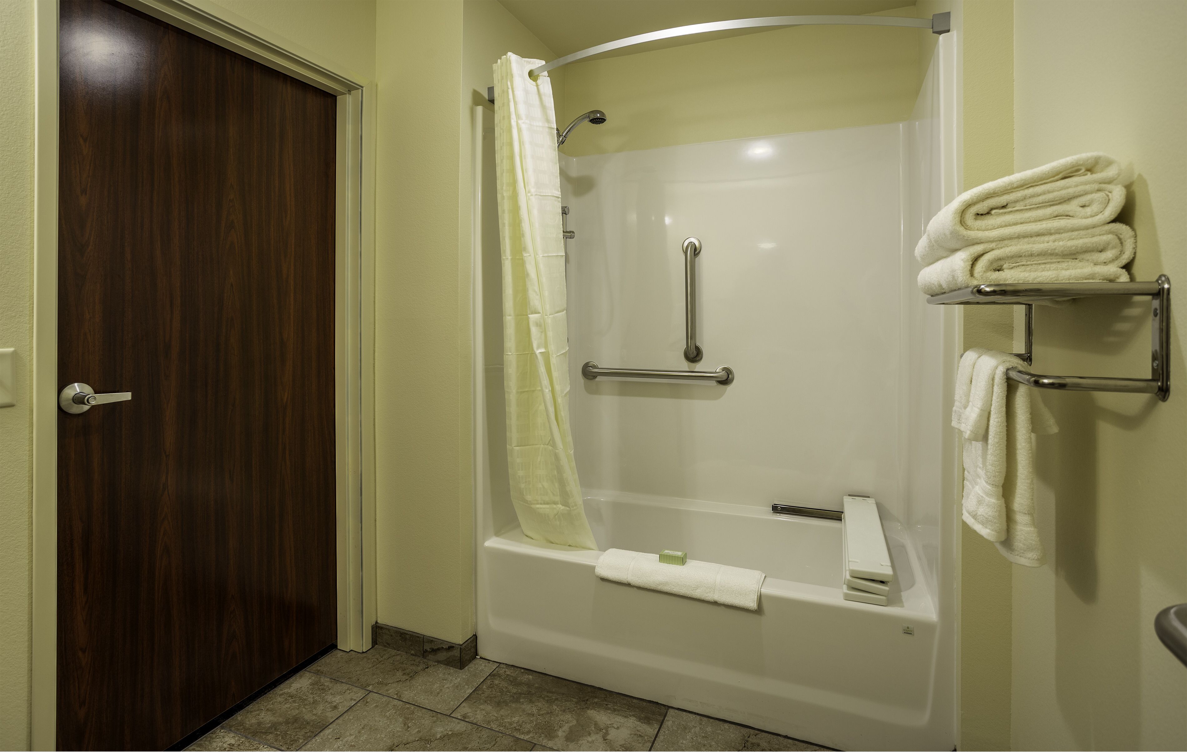 A bathroom with a shower, a toilet, a towel rack, and a door.