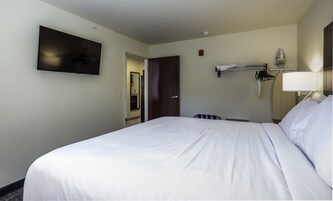 A hotel room with a large bed, a flat-screen TV mounted on the wall, a door leading to a bathroom, and a towel rack with a hanging towel.