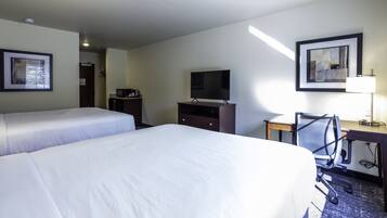 Habitación de hotel con dos camas, un escritorio con silla, televisión, lámpara de escritorio y obras de arte en las paredes.