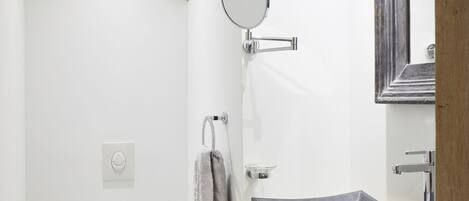 A modern bathroom with a white toilet, a wooden cabinet, a round mirror, and a large sink with a dark countertop.