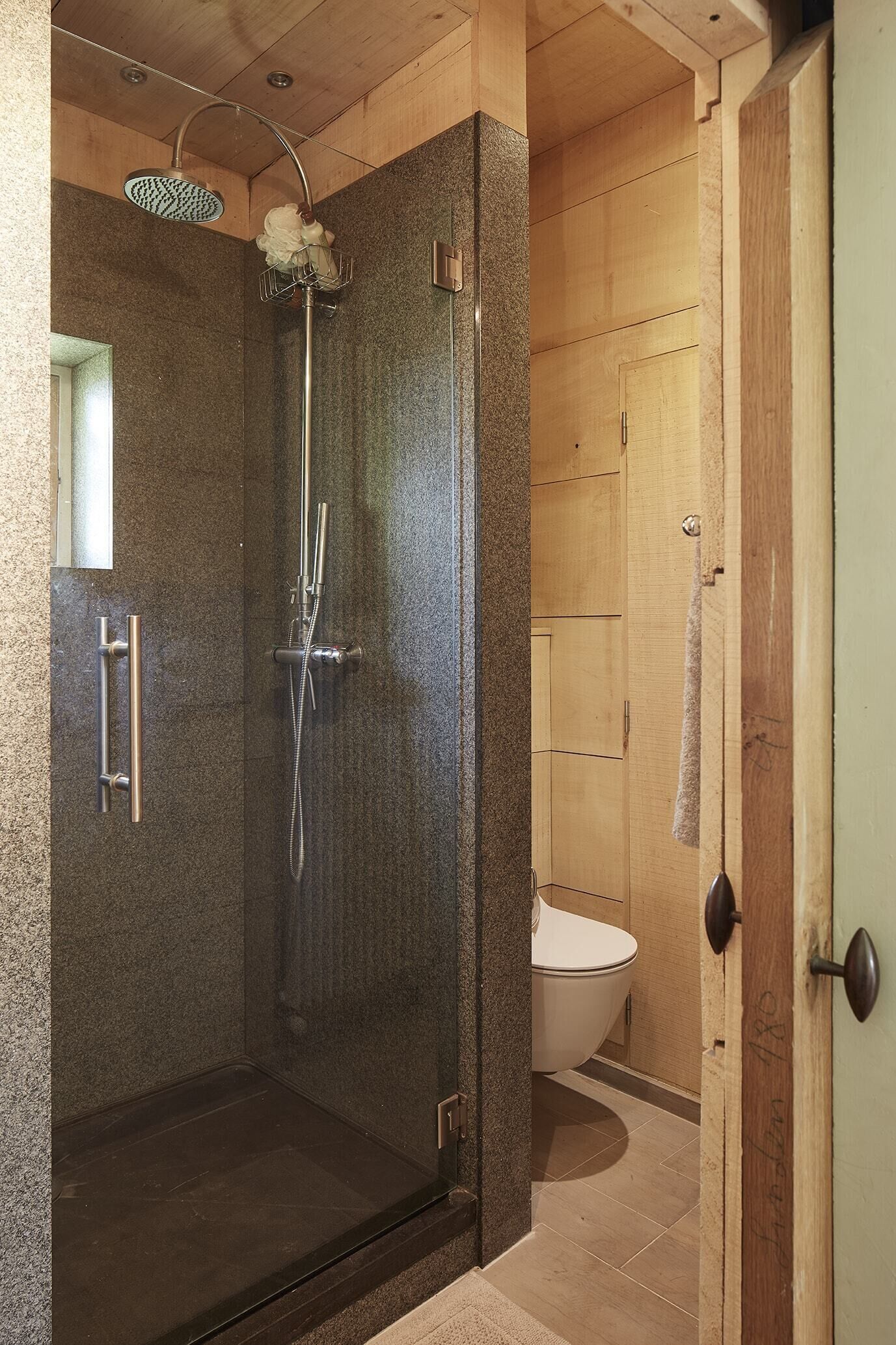 Ducha con paredes de vidrio, cabezal de ducha manual y llave integrada a la pared.