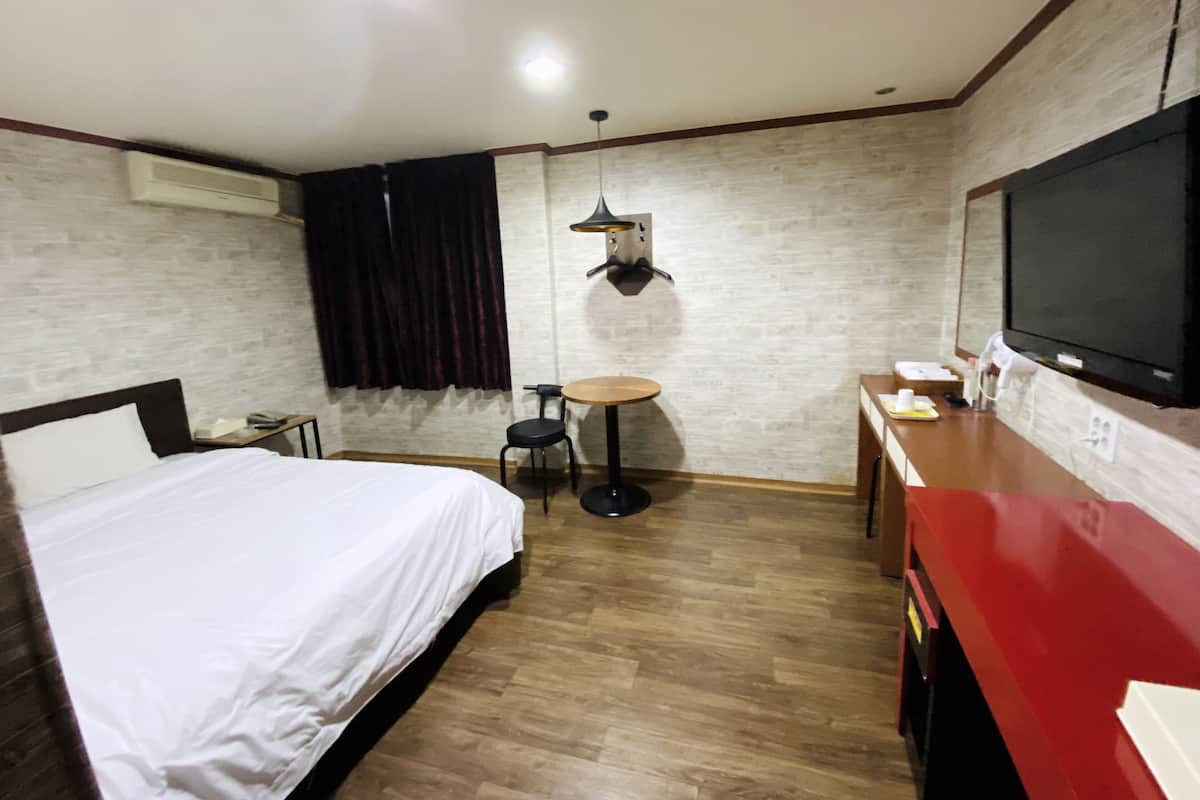 A hotel room with a bed, a desk, a chair, a TV, and a small table.