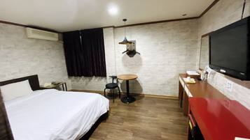A hotel room with a bed, a desk, a chair, a TV, and a small table.