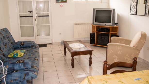 A living room with a sofa, a chair, a coffee table, a television, and a radiator. - Homerez - Apartment in Breuillet (Breuillet)
