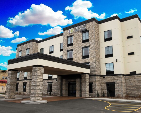 A hotel with a stone facade, a covered entrance, and a parking lot.