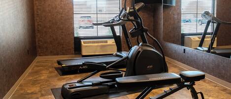 A gym with a treadmill, elliptical, and weight bench.