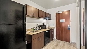 A compact kitchen with a black refrigerator, wooden cabinets, a microwave, and a dishwasher. - Cobblestone Hotel & Suites - Two Rivers (Two Rivers)