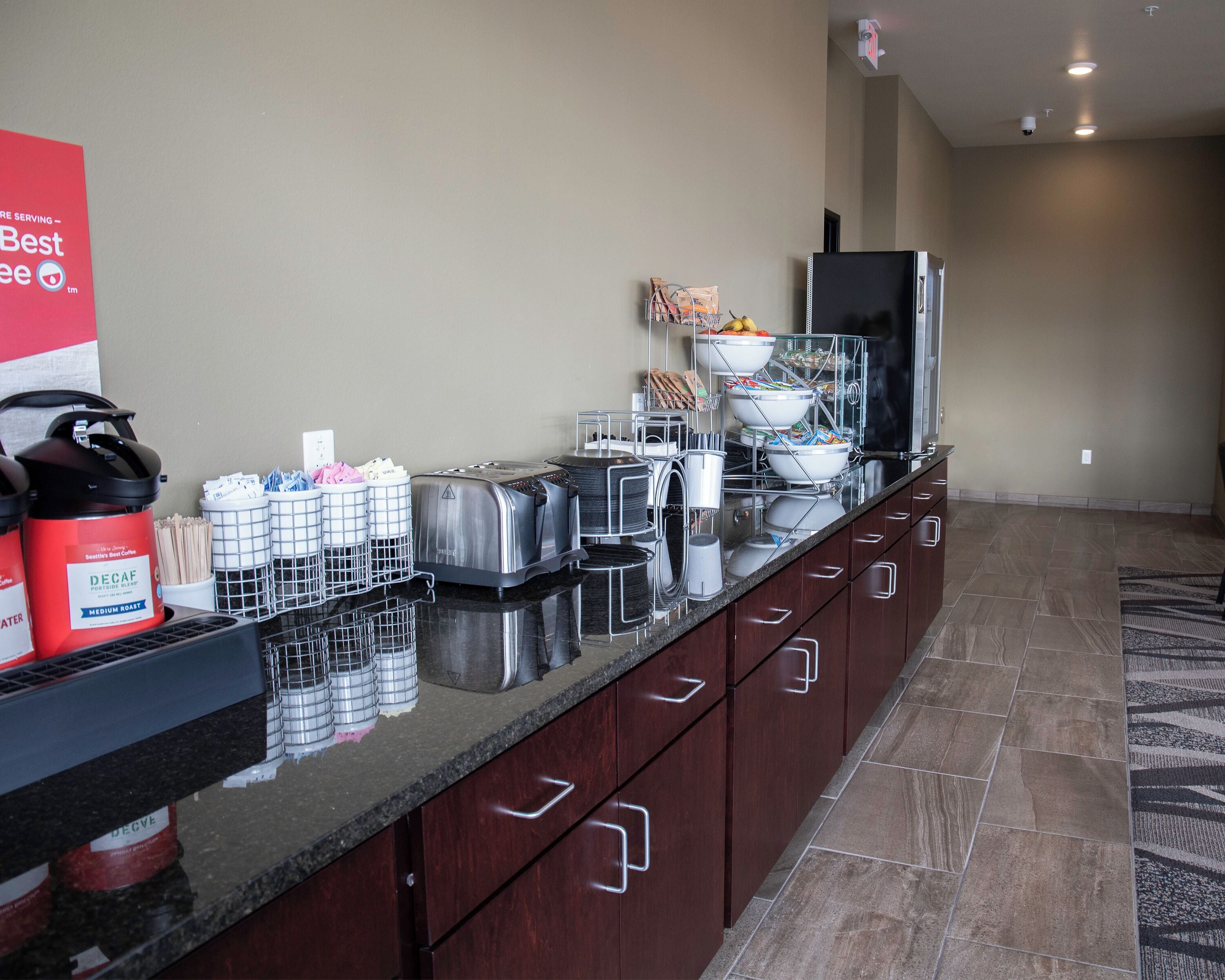 Una cocina de hotel con mesas de buffet, que incluyen cafeteras, tostadoras y un refrigerador.