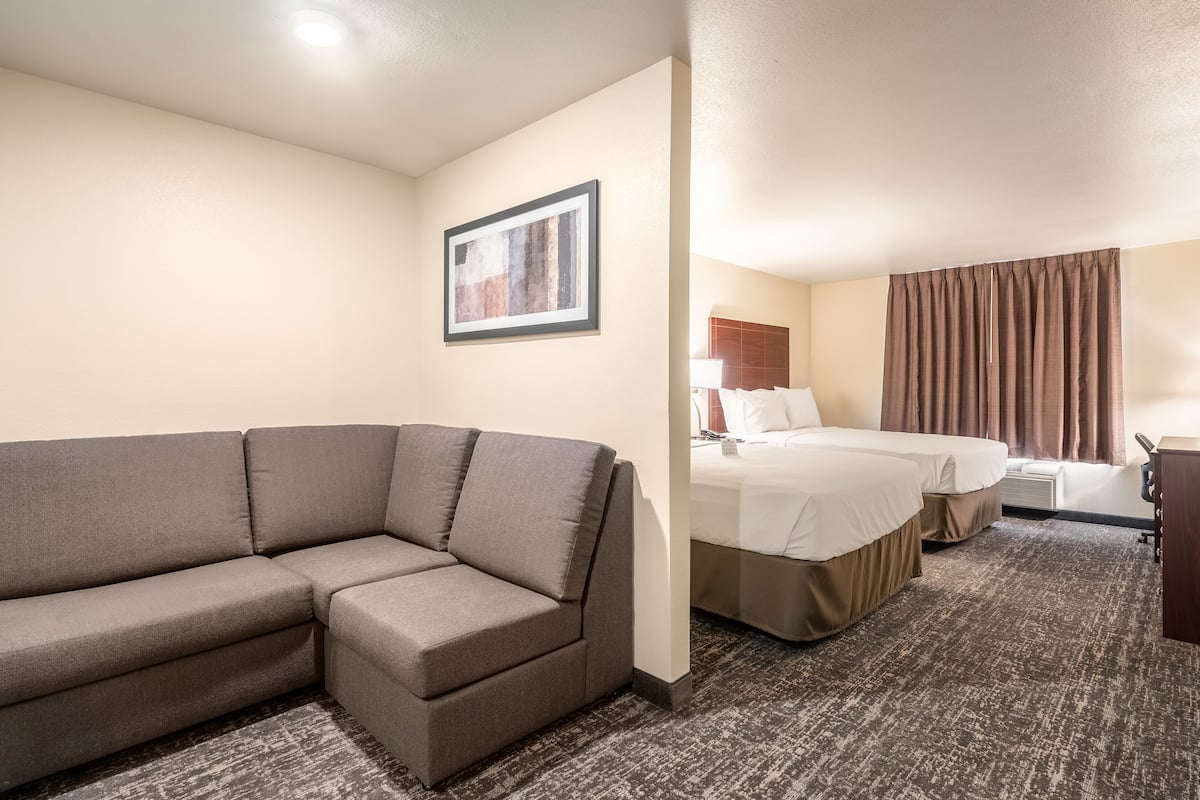 A hotel room with a sofa, two beds, a desk, and a framed picture on the wall.