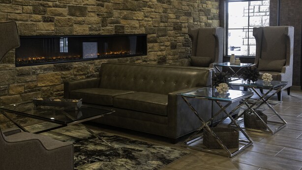 A modern living room with a stone wall, leather sofa, glass coffee table, and a fireplace. - Cobblestone Hotel & Suites - Two Rivers (Two Rivers)