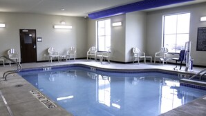 An indoor swimming pool with clear water, surrounded by white chairs and a blue safety sign.