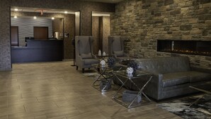 A modern lobby with a stone wall, a fireplace, a reception desk, and a seating area with a sofa and armchairs. - Cobblestone Hotel & Suites - Two Rivers (Two Rivers)
