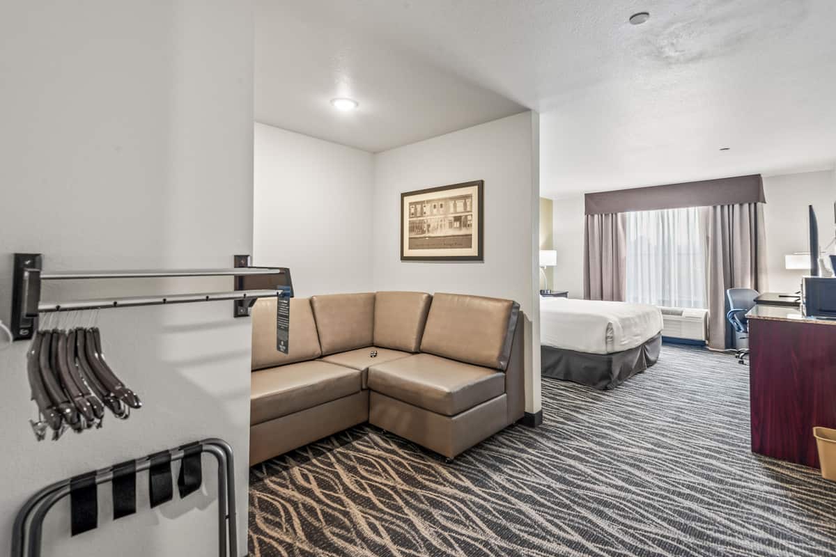 A hotel room with a sectional sofa, a bed, a desk, and a framed picture on the wall.
