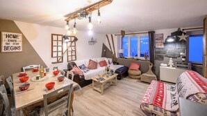 A cozy living room with a wooden dining table set for a meal, a sofa, and a television.