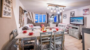 A cozy living room with a dining table set for four, a sofa, a television, and a fireplace.