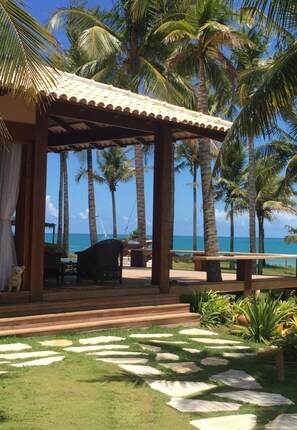 Un espacio al aire libre techado con un pérgola de madera, palmeras y vista al océano.