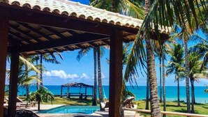 A covered outdoor area with a pool, lounge chairs, and palm trees. - Vila Bela Vista Corumbau (Prado)