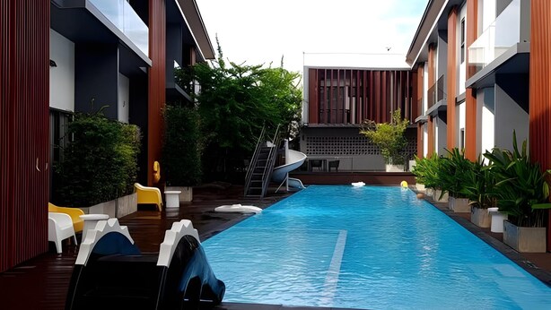 Une piscine avec un toboggan, entourée de bâtiments modernes dotés de balcons et d’un espace de détente extérieur.