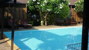 A swimming pool with a wooden deck, lounge chairs, and a covered seating area.