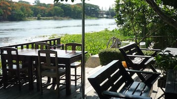 An outdoor deck with wooden tables and chairs, overlooking a river.