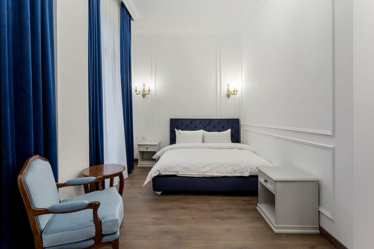 Ein Schlafzimmer mit einem Bett, Nachttischen, einem Sessel und Vorhängen.