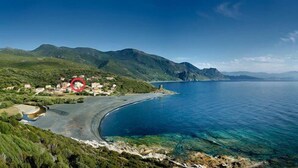 Une zone côtière offrant une vue dégagée sur la mer, un petit village avec des maisons, et des montagnes en arrière-plan.