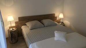 Un lit bien fait, avec une literie à rayures et un oreiller blanc, flanqué de deux tables de chevet avec des lampes, dans une chambre simple dotée d’une tête de lit en bois.