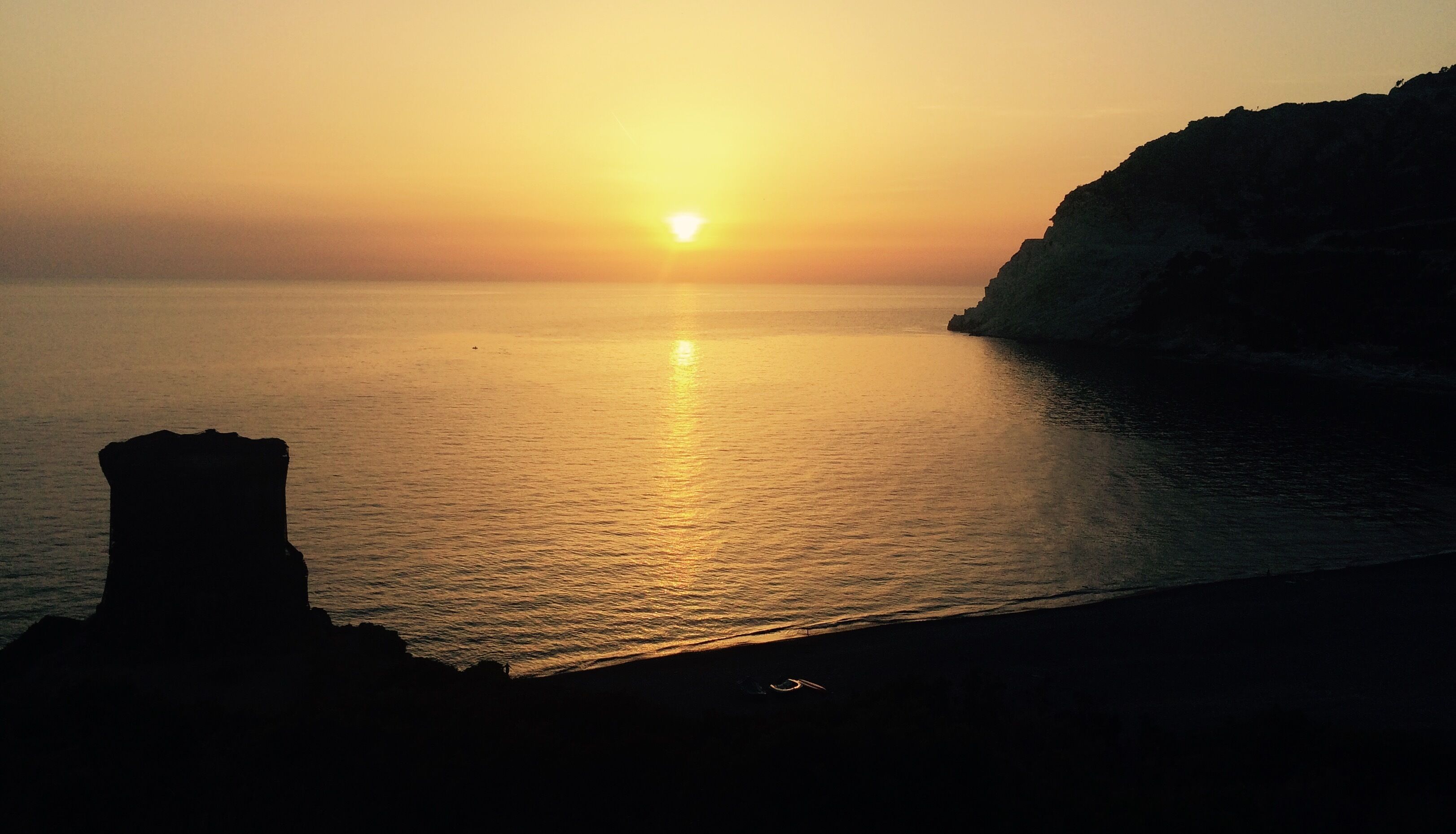 Ein Küsten-Sonnenuntergang mit ruhiger See und Felsen.