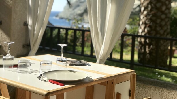 Une table dressée en plein air, avec vue sur la mer, des rideaux blancs et un palmier.