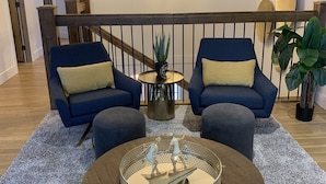 A modern living room with two blue sofas, a round coffee table with a decorative centerpiece, a staircase with a railing, and a hanging light fixture. - Updated house on the Ridge -3 suites, 1 hot tub open for summer, amazing views (Silver Star Mountain)