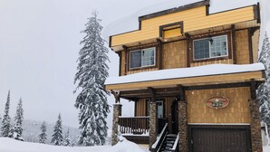A two-story wooden house with a snow-covered roof and a stone foundation. - Updated house on the Ridge -3 suites, 1 hot tub open for summer, amazing views (Silver Star Mountain)