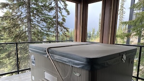 A hot tub with a bench, surrounded by wooden railings, set against a backdrop of trees. - Updated house on the Ridge -3 suites, 1 hot tub open for summer, amazing views (Silver Star Mountain)