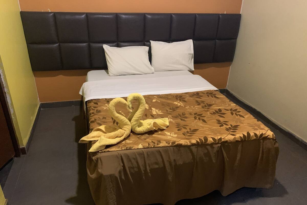 A hotel room with a bed, a headboard, and a decorative swan towel.