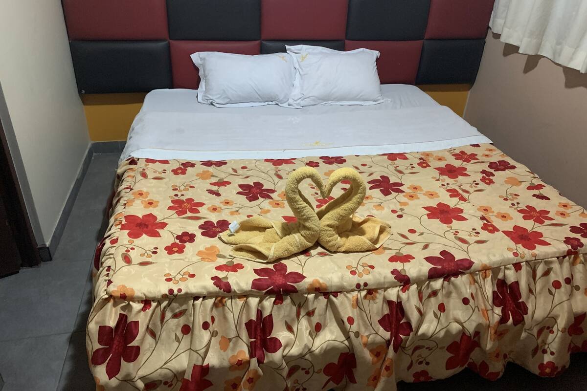 A bed with a floral bedspread, a heart-shaped towel, and a headboard with a checkered pattern.