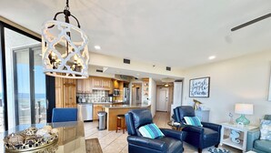 A spacious living area with a large glass table, two leather armchairs, and a modern chandelier.