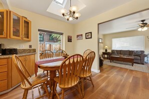 Un coin repas avec une table et des chaises, une cuisine avec des meubles en bois, et un salon avec un canapé et un ventilateur de plafond.