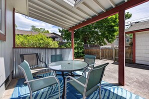 Une terrasse couverte avec une table ronde et des chaises, un tapis à motifs bleus et une clôture en bois en arrière-plan.