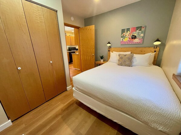 A bedroom with a large bed, wooden wardrobe, and a small bedside table with a lamp. - Federal- AC, In the Heart of Walkable Westside Bend (Bend)