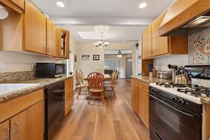 A kitchen with wooden cabinets, a dining table with chairs, a black microwave, a stove, and a dishwasher.