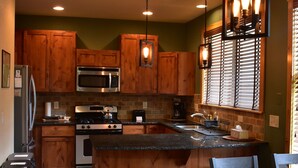 A modern kitchen with wooden cabinets, stainless steel appliances, and a central island with bar stools. - Quiet Loveland Escape – Close to Downtown, Parks & I-25 (Loveland)