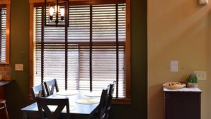 A dining area with a wooden table and chairs, a pendant light, and a window with blinds. - Quiet Loveland Escape – Close to Downtown, Parks & I-25 (Loveland)