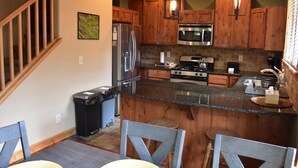 A kitchen with wooden cabinets, stainless steel appliances, granite countertops, and a dining area with chairs. - Quiet Loveland Escape – Close to Downtown, Parks & I-25 (Loveland)