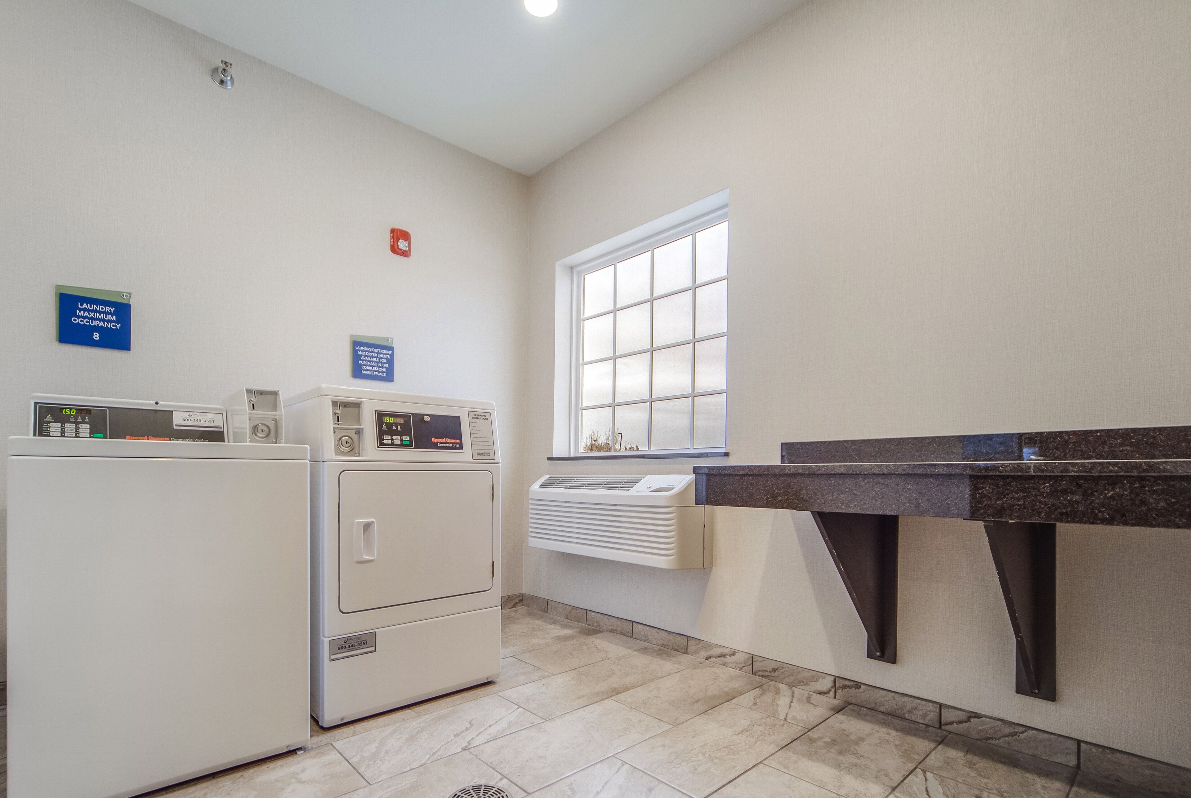 A laundry room with two front-loading washers and dryers, a window, and a countertop with a sink.