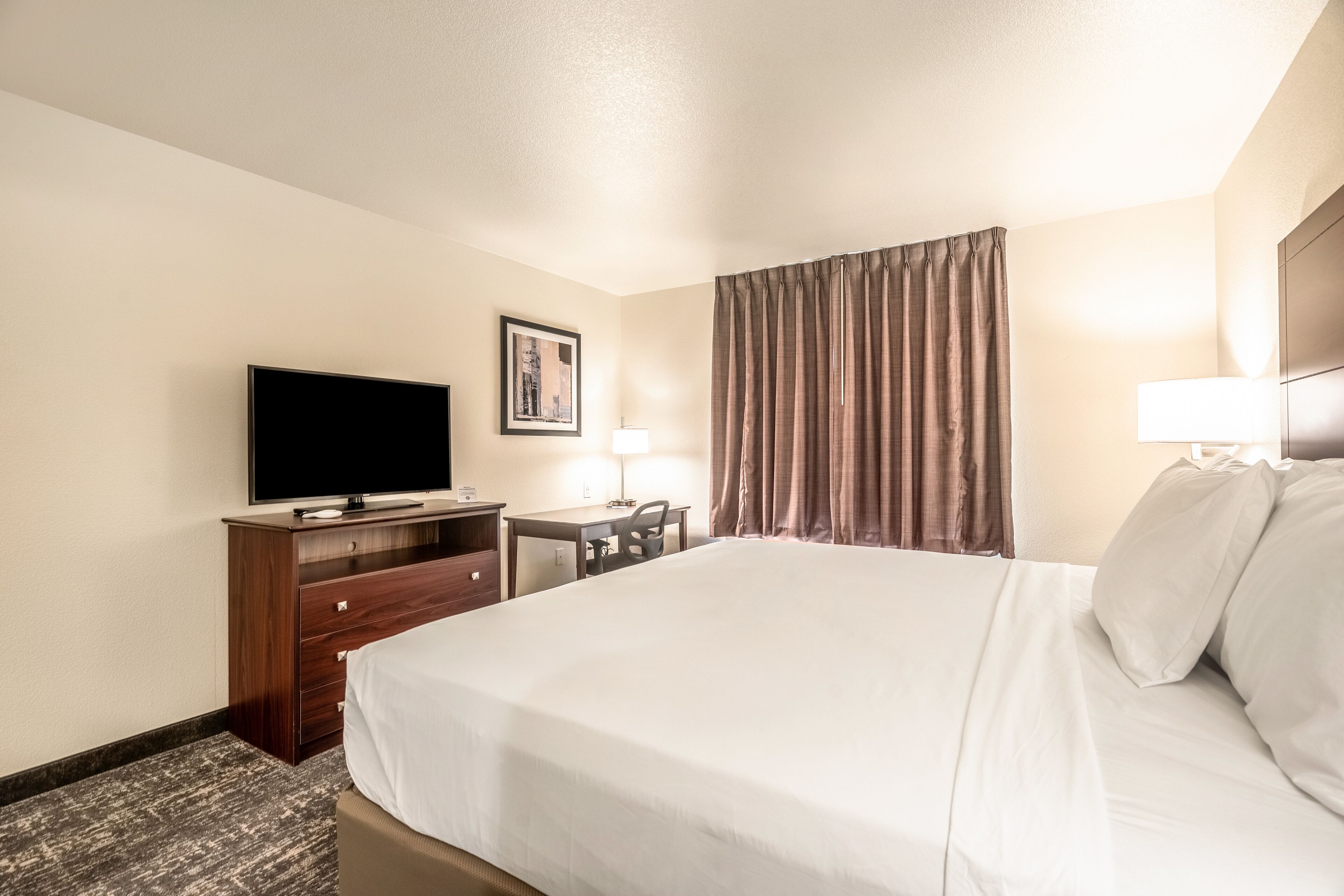 A hotel room with a bed, a desk, a chair, a television, and a window with curtains.