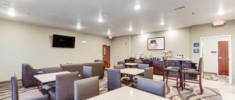 A hotel lobby with seating areas, a reception desk, and a television mounted on the wall.