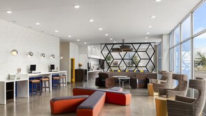 Un área de estar moderna con asientos, una cocina y ventanas amplias.